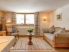 Wohnzimmer mit Möbeln und Fenster in einem Haus In einem Raum stehen ein Sofa und ein Sessel. Ein Tisch mit Pflanzen steht in der Mitte. Es gibt ein Fenster mit Licht.