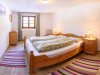Schlafzimmer mit Doppelbett und Holzdekor In einem Raum steht ein großes Bett mit zwei Kissen. Der Boden hat bunte Teppiche. Fenster lassen Licht herein.