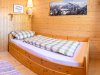 Ein Zimmer mit einem Bett und einem Fenster In einem Holzraum steht ein Bett mit einer Decke. Im Hintergrund sind Berge und ein Bild an der Wand.
