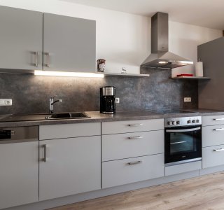 Bild von einer der Küchenzeilen mit Herd, Kaffeemaschine, Backofen und Kühlschrank.