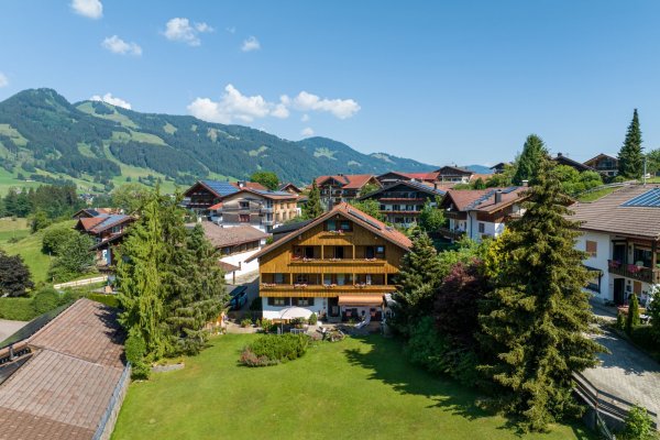 Blick auf ein Dorf in den Bergen von Bayern Das Dorf liegt in den Bergen, zwischen Bäumen und Bergen. Die Sonne scheint und der Himmel ist blau.