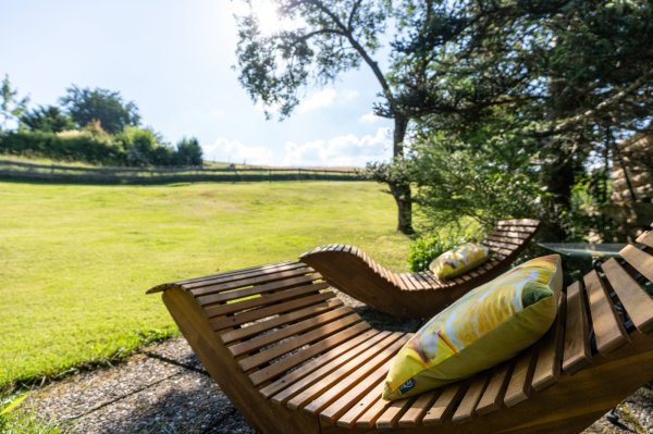 Entspannung auf einer Liege im Garten Jemand sitzt auf einer Holzliege im Garten. Die Sonne scheint und der Rasen ist grün. Es gibt Kissen auf der Liege.