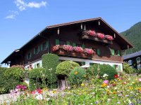 Bunt blühendes Haus in den Bergen Ein schönes Holzhaus mit bunten Blumen im Vordergrund liegt in einer malerischen Berglandschaft unter blauem Himmel.