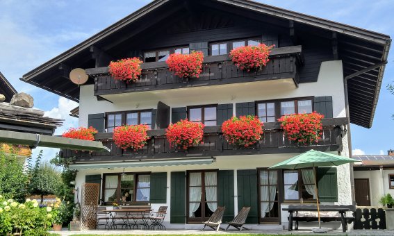 Ein einladendes Gebäude in den Alpen mit blühenden Blumenkästen und einem gepflegten Garten an einem sonnigen Tag.