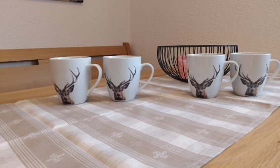 Auf einem Tisch stehen vier Tassen mit Hirschmotiven. Daneben ist ein Korb mit Bällen zu sehen.