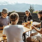 Gemeinsame Hüttenzeit Entspannte Wanderpause auf der Hörnerhaus-Sonnenterasse mit Kartenspielen und kühlen Getränken.