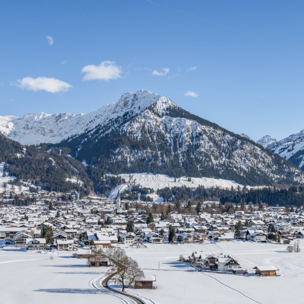 Schneebedecktes Dorf in Winterlandschaft mit Bergen im Hintergrund Eine ruhige Winterlandschaft mit schneebedeckten Bergen und einem kleinen Dorf, umgeben von Natur.