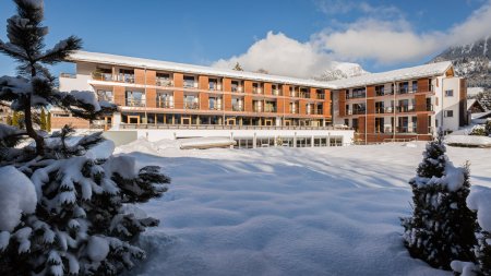 Ein modernes Hotel steht in einer verschneiten Landschaft. Die Sonne scheint auf die schneebedeckten Flächen des Winters.