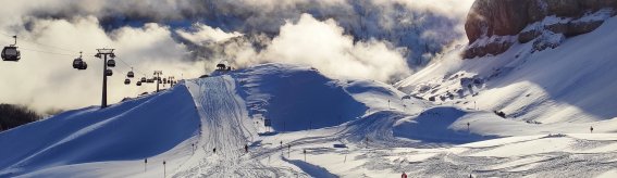 Eine schneebedeckte Berge mit einem Skilift und der Sonne, die hinter den Wolken aufgeht. Klare Himmel und winterliche Stille.
