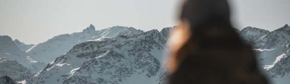 Eine Person steht im Vordergrund und betrachtet majestätische schneebedeckte Berge bei klarem Wetter im Winter.