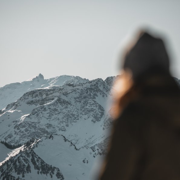 Eine Person steht im Vordergrund und betrachtet majestätische schneebedeckte Berge bei klarem Wetter im Winter.