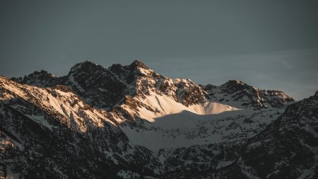 Die schneebedeckten Berge leuchten im Abendlicht. Die Wolken sorgen für eine dramatische Stimmung in der Landschaft.