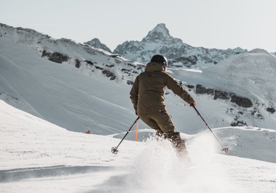 Ein Skifahrer gleitet durch den frischen Schnee in den Alpen unter blauem Himmel.