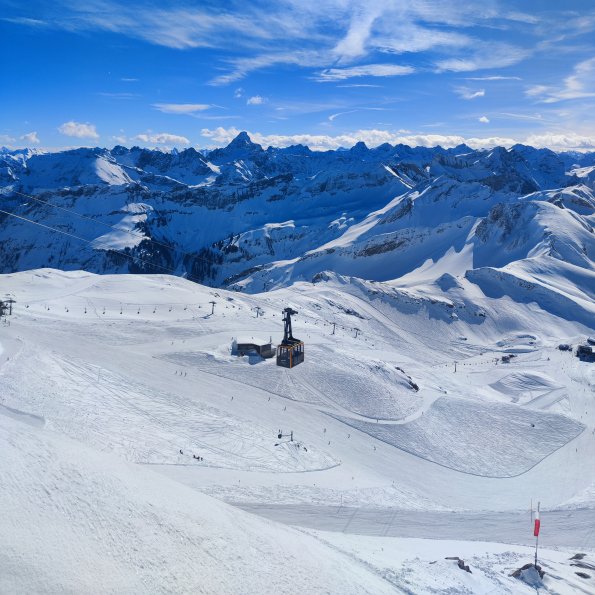 Die schneebedeckten Berge strahlen unter blauem Himmel im Winter. Die Nebelhornbahn steht im Vordergrund.