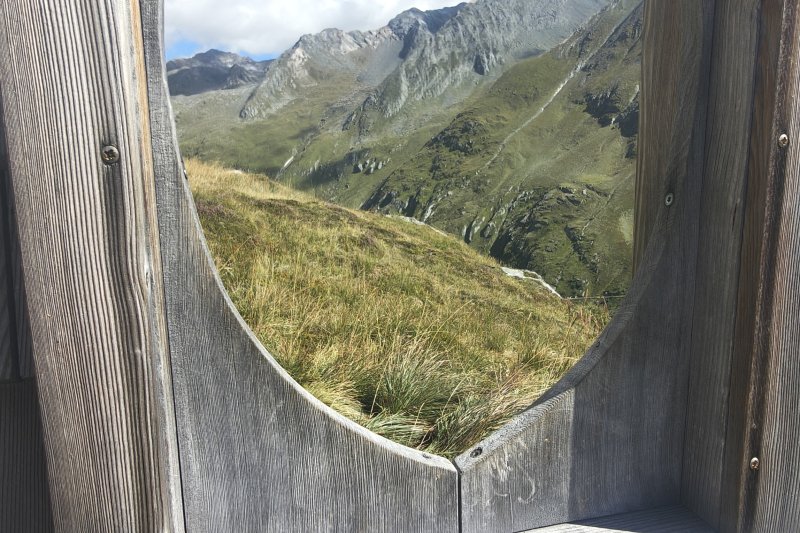 Ausblick aus der HEIMAT ins Virgental bei Prägraten am Großvenediger. Durch das Fenster eröffnet sich der Blick auf die beeindruckende Bergwelt Osttirols und den Nationalpark Hohe Tauern. Ein besonderer Moment für alle, die im Urlaub Ruhe, Natur und die Berge genießen möchten.