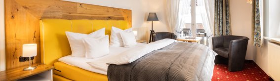 Das Zimmer zeigt ein gelbes Bett und zwei Stühle. Es gibt ein Fenster und einen Tisch im Raum.