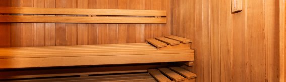 In einer Sauna aus Holz sind Regale zu sehen. Ein Eimer steht bereit. Es ist ruhig und warm in diesem Raum.
