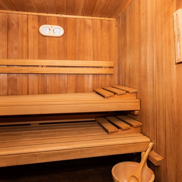 In einer Sauna aus Holz sind Regale zu sehen. Ein Eimer steht bereit. Es ist ruhig und warm in diesem Raum.