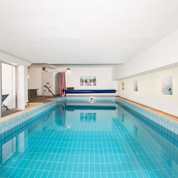 Schwimmbad in einem Innenraum Das Schwimmbad ist drinnen. Das Wasser ist blau. Es gibt Liegen neben dem Becken. Es ist ein ruhiger Ort.