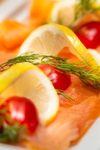 Auf einem Teller liegen Scheiben von frischem Lachs, garniert mit Zitronen und Kirschtomaten. Die Aufnahme zeigt eine Übersicht der Speise.