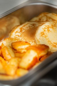 Es sind Pancakes und gebratene Äpfel in einer Schale zu sehen. Das Essen ist warm und bereit zum Servieren.