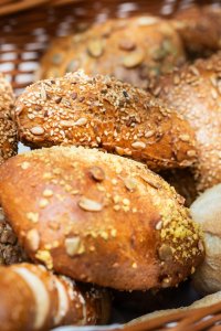 Ein Korb voller frischer Brötchen und Brote steht auf einem Tisch. Die Brötchen haben verschiedene Samen und eine goldene Farbe.