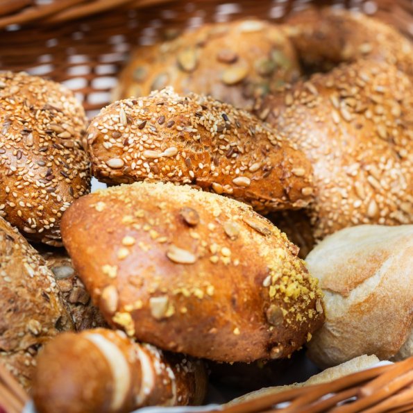 Brot und Brötchen in einem Korb Ein Korb voller frischer Brötchen und Brote steht auf einem Tisch. Die Brötchen haben verschiedene Samen und eine goldene Farbe.
