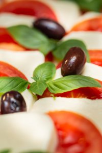 Auf einem weißen Teller liegen Scheiben von Tomaten und Mozzarella, garniert mit Basilikum und Oliven.