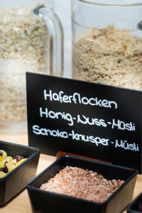 Auf einem Tisch stehen Gläser mit verschiedenen Müslizutaten. Darunter sind Haferflocken und Trockenfrüchte.