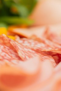 Auf einem Tisch sind verschiedene Arten von Aufschnitt und frische Kräuter angeordnet. Die Szene zeigt eine appetitliche Anordnung.