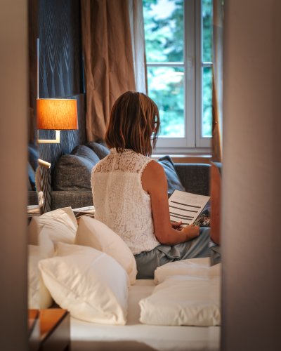 Erholung pur im Hotel Mohren in Oberstdorf: In stilvollem Ambiente entspannen Gäste im komfortablen Zimmer und blättern entspannt in der Gästemappe. Perfekt für eine Auszeit im Allgäu mit Wohlfühlgarantie.