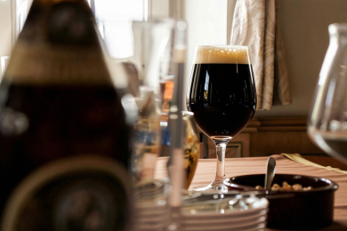 Auf einem Tisch steht ein Biertulpe mit dunklem Craft-Bier.