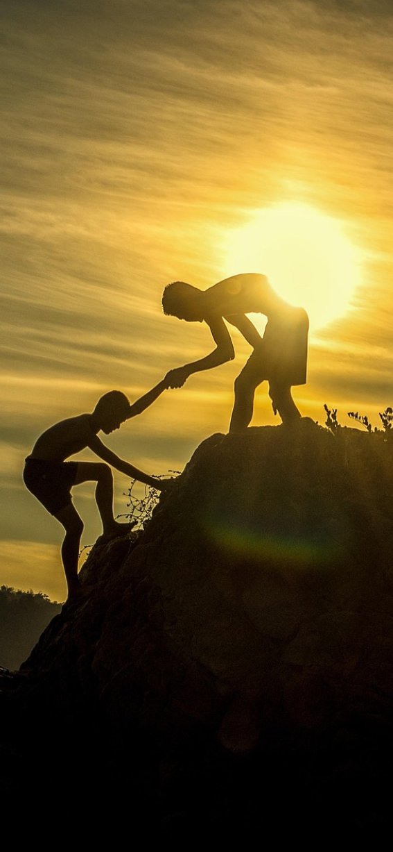 Zwei Personen assistieren sich gegenseitig beim Klettern auf einen Felsen während des Sonnenuntergangs in der Natur.