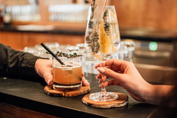 Drinks und Genuss an der Kaminbar im Hotel Oberstdorf Zwei Gäste stoßen mit Cocktails an der Kaminbar des Hotel Oberstdorf an – entspannte Genussmomente in gemütlicher Atmosphäre.