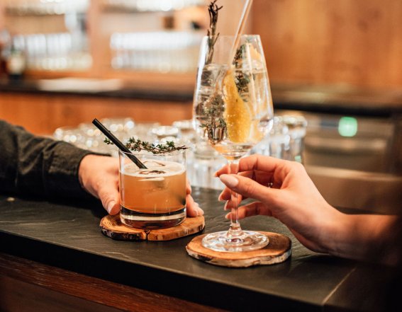 Drinks und Genuss an der Kaminbar im Hotel Oberstdorf Zwei Gäste stoßen mit Cocktails an der Kaminbar des Hotel Oberstdorf an – entspannte Genussmomente in gemütlicher Atmosphäre.