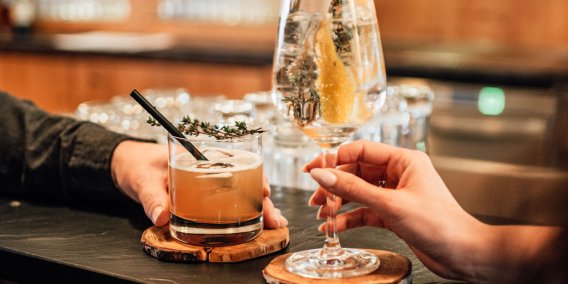 Drinks und Genuss an der Kaminbar im Hotel Oberstdorf Zwei Gäste stoßen mit Cocktails an der Kaminbar des Hotel Oberstdorf an – entspannte Genussmomente in gemütlicher Atmosphäre.