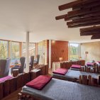 Gemütlicher Panorama-Ruheraum in der Alpen Wellnesswelt des Hotel Oberstdorf mit großen Fenstern, Liegeflächen und Blick ins Grüne.