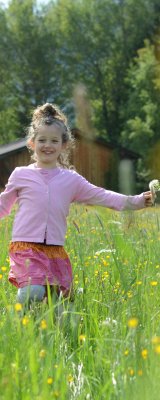 Ein tollendes Mädchen auf einer grünen Sommerwiese. Im Hintergrund die umliegenden Berge der Allgäuer Alpen in Oberstdorf und Umgebung.