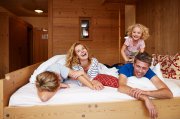 Familie lacht gemeinsam auf dem Bett in einem Familienzimmer im Hotel Oberstdorf Wenn man im Urlaub näher zusammenrückt und endlich viel Zeit für die Familie hat, dann muss natürlich auch mal richtig getobt werden.