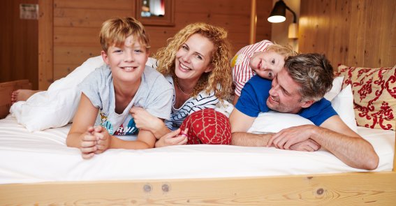 Familie genießt gemeinsame Zeit auf dem Bett im Familienzimmer des Hotel Oberstdorf Sie sind gemütlich und bieten Platz für die ganze Familie - die Zimmer im Hotel Oberstdorf im Allgäu.