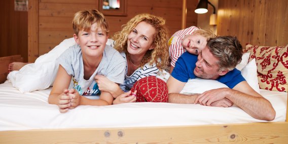 Familie genießt gemeinsame Zeit auf dem Bett im Familienzimmer des Hotel Oberstdorf Sie sind gemütlich und bieten Platz für die ganze Familie - die Zimmer im Hotel Oberstdorf im Allgäu.