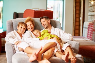Familie kuschelt im Bademantel auf einem Sessel im Wellnessbereich des Hotel Oberstdorf Wellness im Allgäu, Familienzeit im Hotel