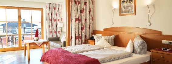 Ein Schlafzimmer mit zwei Betten, einem Tisch und Fenstern, die auf eine Terrasse führen. Es ist hell und einladend.