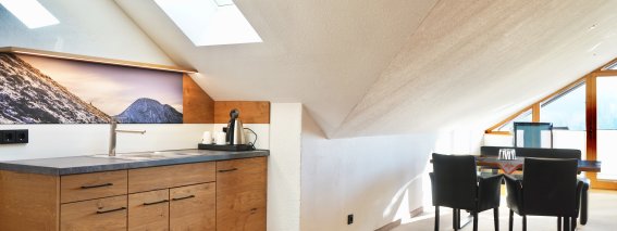 In einem Dachgeschoss befindet sich eine kleine Küche mit einem Tisch und einem Stuhl. Es gibt Fenster und eine Aussicht.