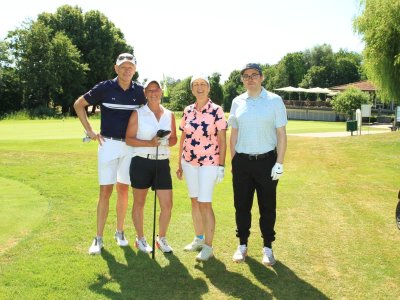 Vier Personen stehen auf dem Golfplatz und halten Schläger. Der Himmel ist blau und die Sonne scheint.