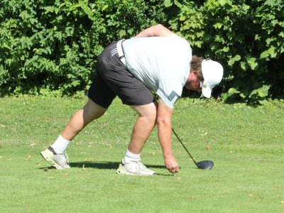 Eine Person beugt sich runter und hebt den Golfball auf einem Golfplatz in der Sonne.