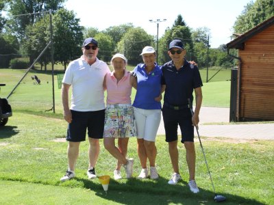 Vier Personen stehen auf einem Golfplatz und lächeln. Es ist ein sonniger Tag und sie tragen bequeme Kleidung.