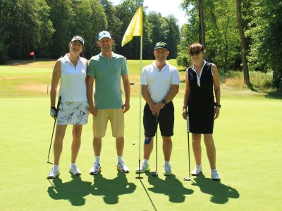 Vier Personen stehen auf dem Golfplatz. Sie tragen Golfkleidung und schauen in die Kamera. Der Tag ist sonnig.