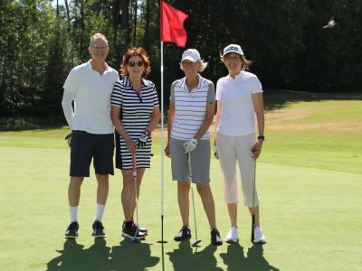 Vier Personen stehen auf dem Golfplatz vor einer roten Fahne. Es ist sonnig und sie halten Golfschläger.