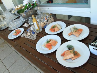 Auf einem Tisch im Freien stehen Teller mit Fischgerichten. Der Tisch hat Gläser, Besteck und Getränke.